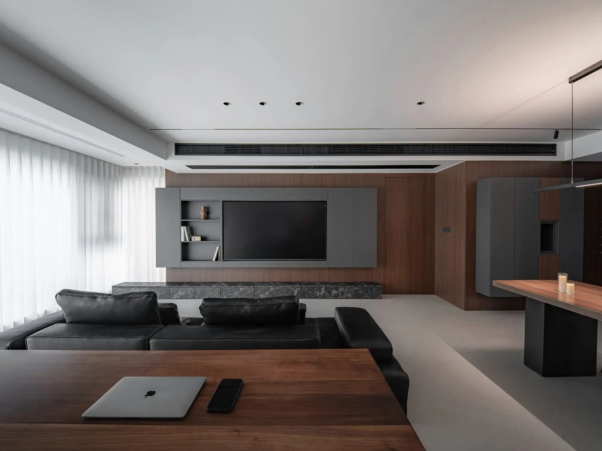 Sala com painel de TV em marcenaria grafite e mesa de madeira.