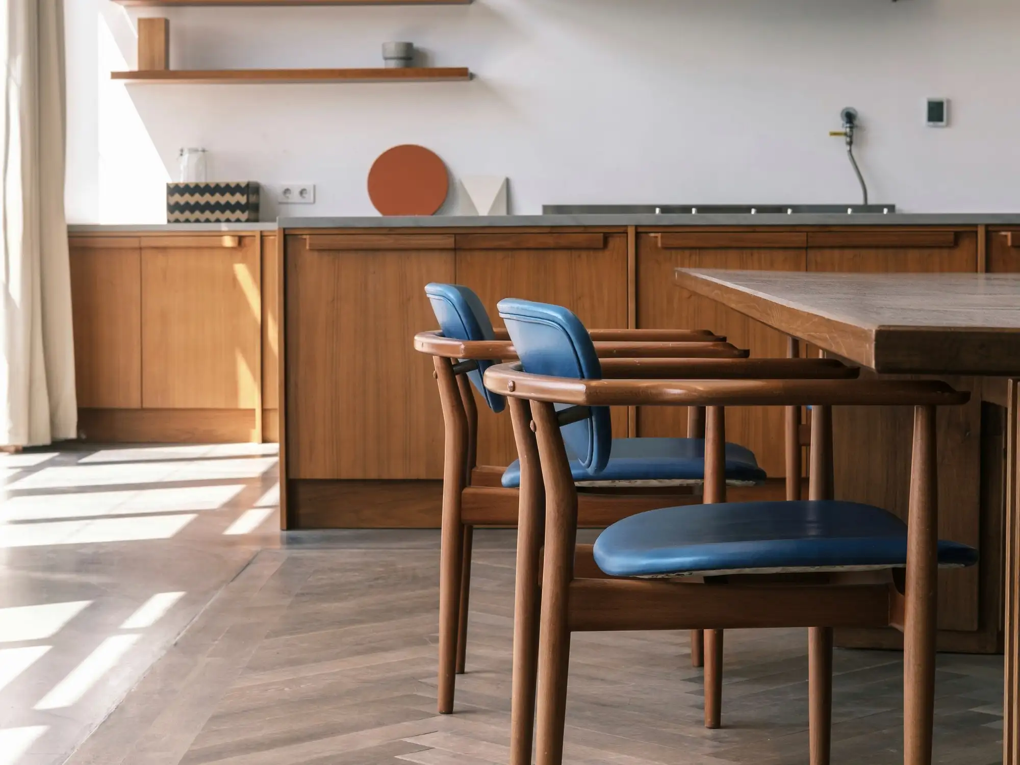 Cozinha em madeira com mesa e cadeiras de assento azul sobre piso em espinha de peixe.